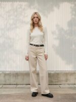 Femme blonde portant un haut beige et un jean baggy beige tendance, sur fond clair