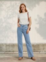 Femme rousse portant un t-shirt beige et un jean droit bleu ciel, sur fond clair