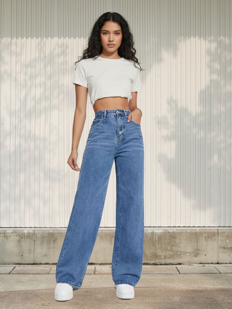 Femme brune portant un crop top blanc avec un jean droit bleu et taille haute, sur fond clair
