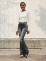 Femme noire portant un haut blanc et un jean flare gris délavé, sur fond clair