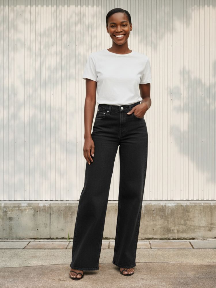Femme noire portant un t-shirt blanc et un jean flare noir wide leg, sur fond clair