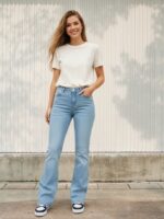 Femme portant un t-shirt beige et un jean bootcut bleu ciel taille haute délavé, sur fond clair