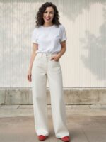 Femme brune portant un t-shirt blanc et un jean blanc taille haute et à coupe large, sur fond clair