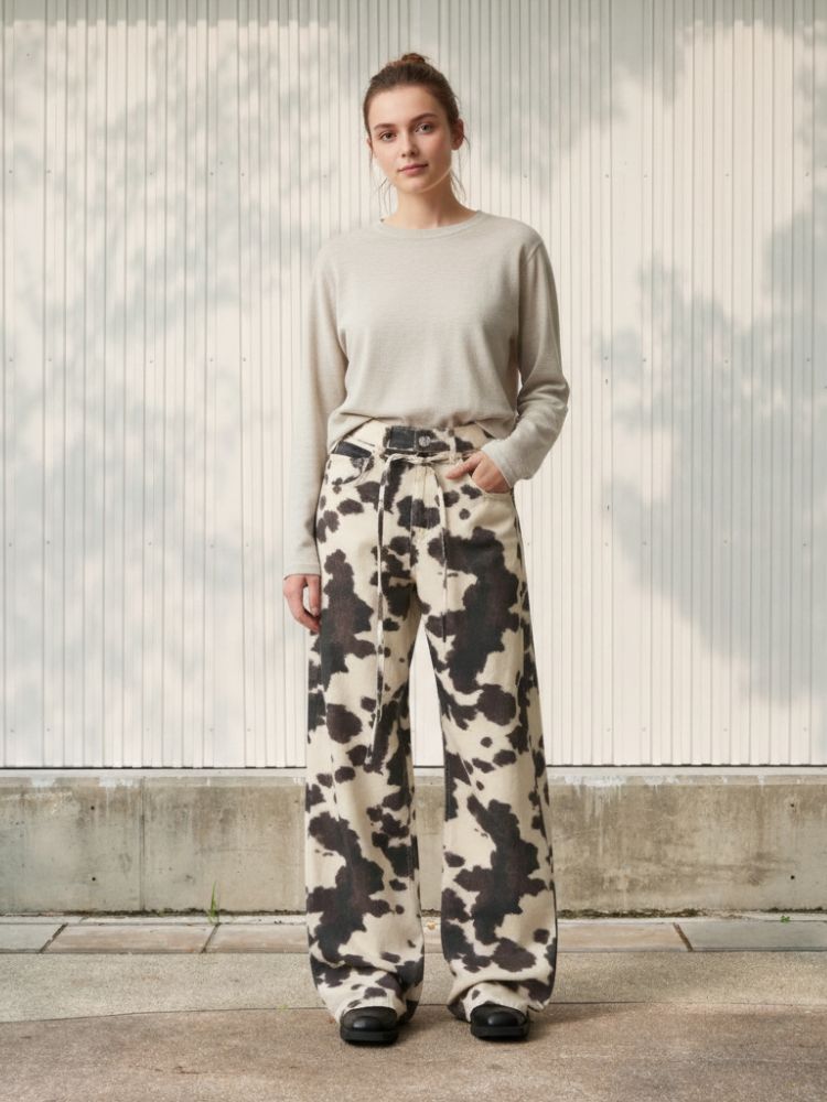 Femme portant une blouse beige avec un jean ample au style vintage et à imprimé vache blanc et marron, sur fond clair