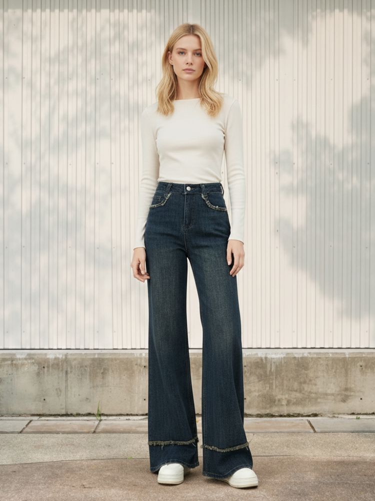 Femme blonde portant un haut blanc et un jean taille haute bleu foncé au style vintage, sur fond clair