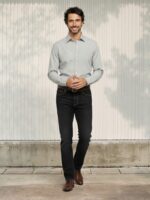 Homme caucasien brun portant une chemise manche longue grise et un jean droit nor stretch élégant et souple avec chaussure marron dans un lieu ensoleillé.