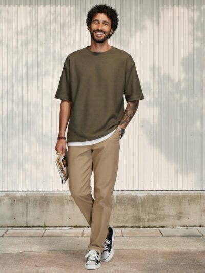 Homme au teint et aux cheveux bruns portant un t-shirt oversize vert et un jean fuselé en denim beige avec finitions artisanales dans un lieu éclairé et ensoleillé.