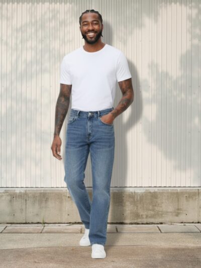 Homme de couleur portant un t-shirt blanc et un jean regular homme effet usé bleu sur fond clair et ensoleillé.