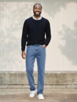 Homme de couleur portant un pull en maille classique bleu marine, un jean regular aux teintes de classique bleu sur fond très éclairé.