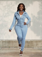 Femme portant une combinaison en jean bleu ciel avec des franges style western, sur fond clair
