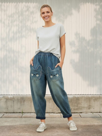 Femme portant un t-shirt blanc avec un jean ballon bleu délavé avec des poches chats adorables, sur fond clair