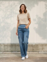 Femme enceinte portant un t-shirt beige avec un jean de grossesse bleu à poches utilitaires d'inspiration cargo, sur fond clair