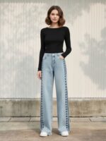 Femme portant un haut noir à manches longues avec un jean taille haute bleu ciel avec des broderies, sur fond clair