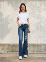 Femme portant un t-shirt blanc et un jean flare au style vintage, avec des broderies de fleurs blanches, sur fond clair
