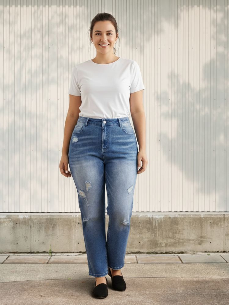 Femme ronde portant un t-shirt blanc et un jean bleu délavé et troué, sur fond clair