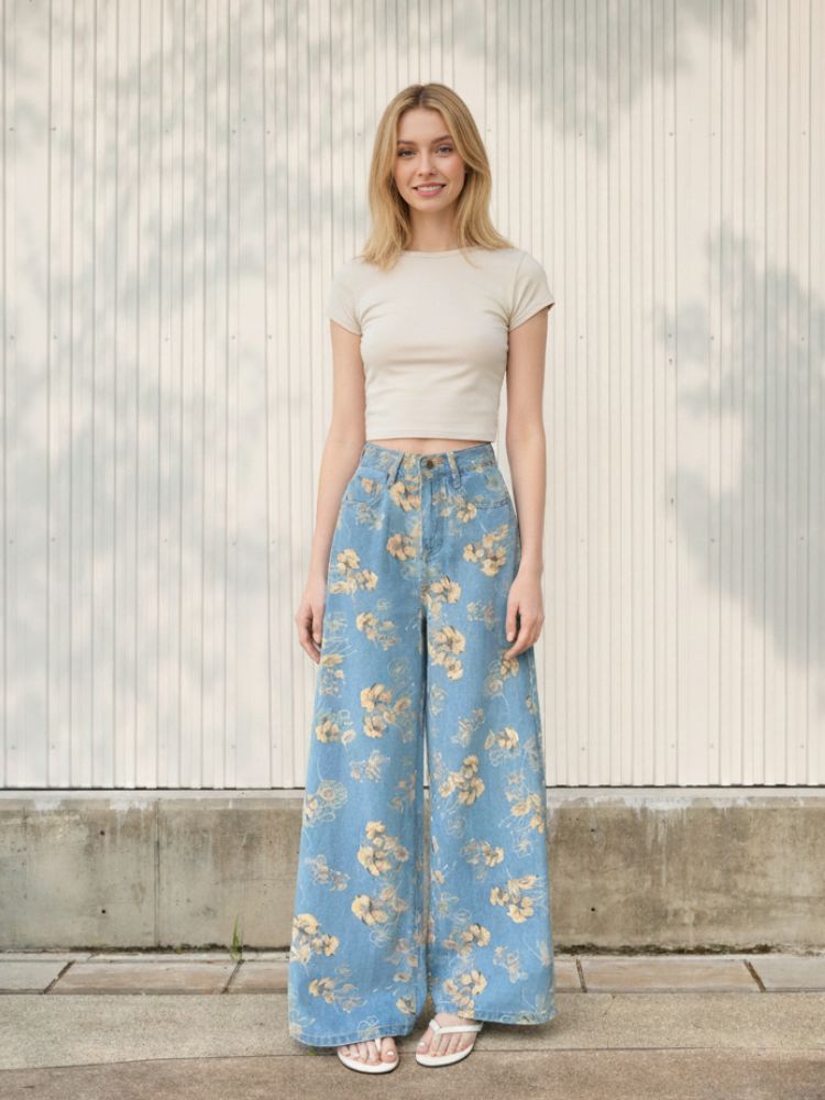 Femme blonde portant un t-shirt blanc et un jean vintage bleu ciel à imprimé fleurs, coupe large, sur fond clair