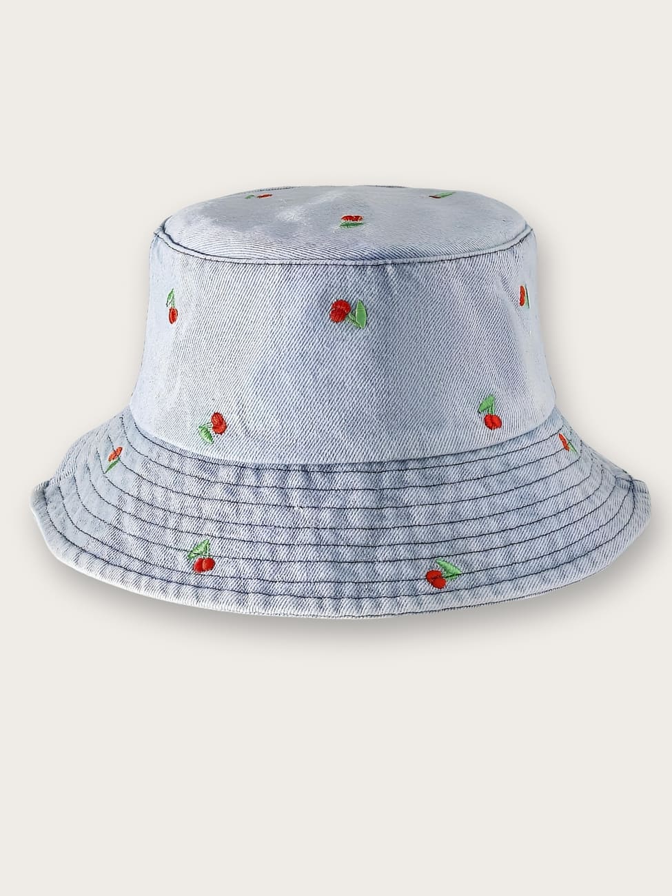 Bob en jean femme avec motifs de cerises. Le bob est de couleur bleu clair sur fond beige.