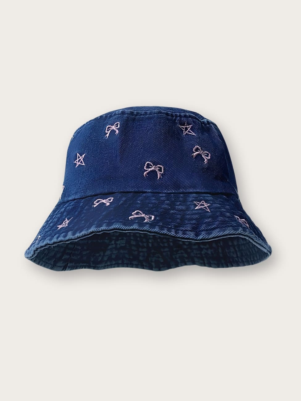 Bob en jean pour femme avec motifs de nœuds et étoiles. Le bob est de couleur bleu foncé sur fond beige. Les motifs sont roses pastel.