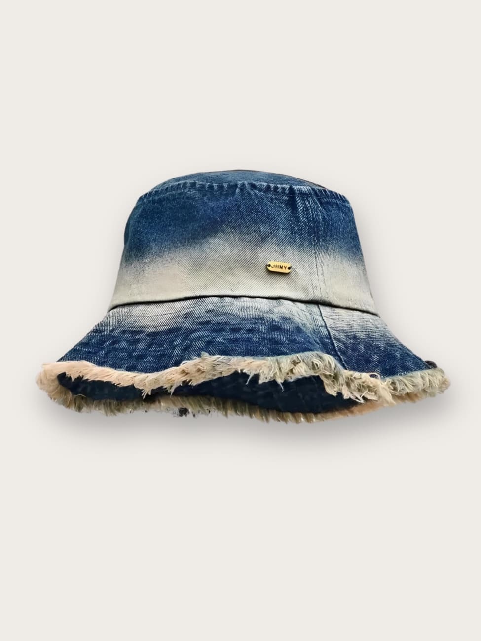 Bob en jean pour femme effet délavé à bords effilochés. De couleur bleue avec une bande plus claire au milieu, les bords effilochés sont beiges. Sur fond beige.