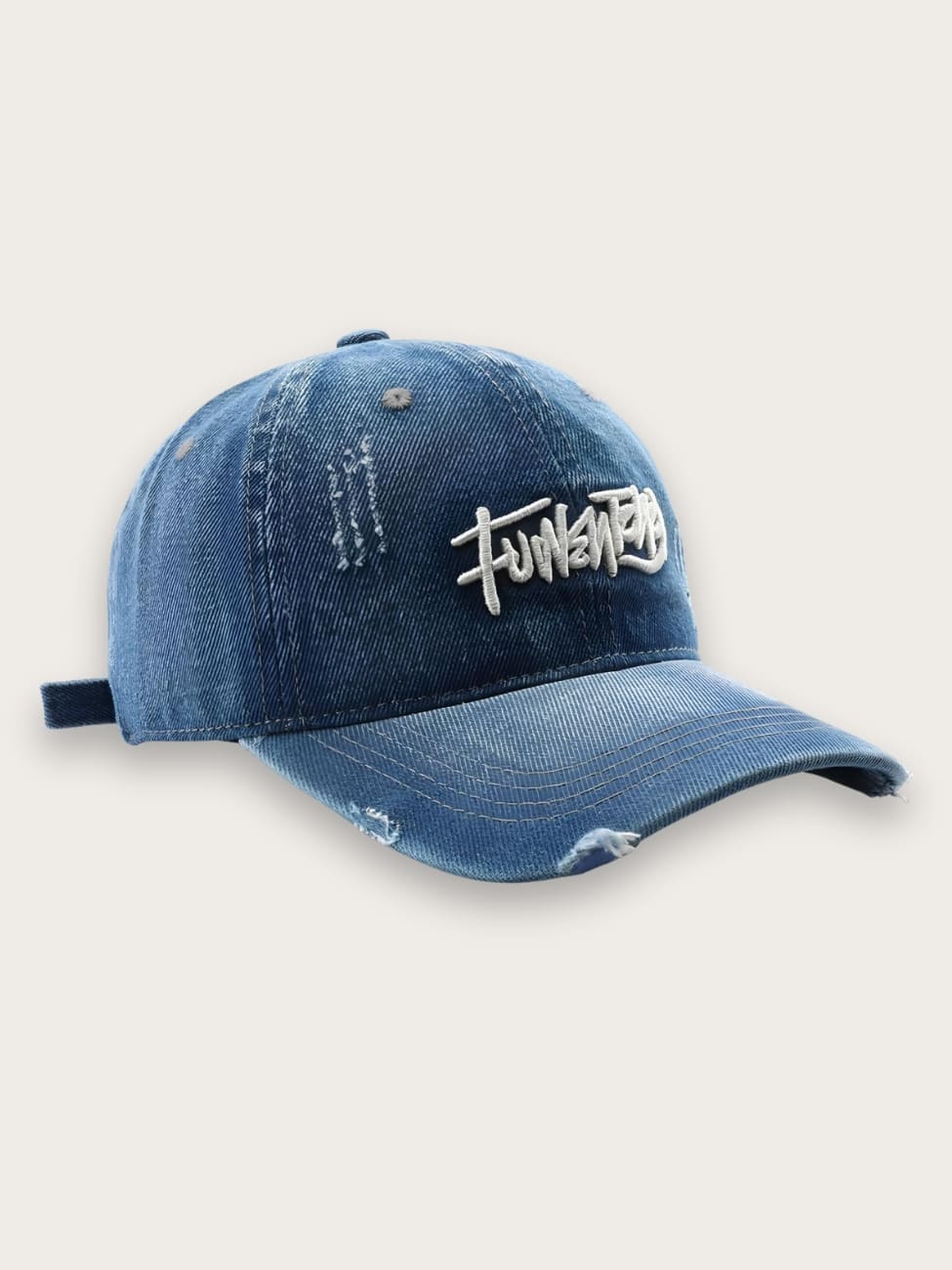 Casquette en jean denim déchiré pour homme de couleur bleu avec des déchirures sur la visière courbée, une inscription style tag blanc. Sur fond beige.