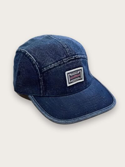Casquette en jean homme style vintage de couleur bleu foncé avec un encart brodé sur l'avant. Sur fond beige.