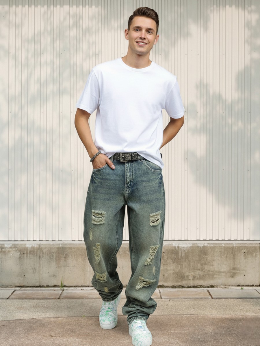 Jeune homme caucasien vêtu d'un t-shirt blanc, et d'un jean baggy effet destroy bleu délavé en denim robuste