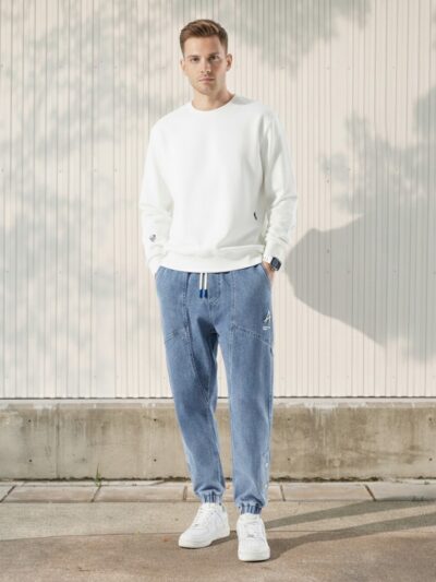 Homme caucasien portant un pull blanc manches longues et un jean jogger, taille élastique et boutons-pression sur fond clair.