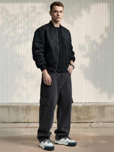 Homme caucasien habillé d'une veste courte noire, d'un t-shirt noir et d'un jean cargo noir chiné aux coutures apparentes dans un lieu clair.