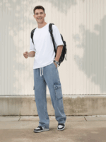 Un jeune homme souriant habillé d'un t-shirt blanc et d'un jean cargo à taille élastique, coupe ample polyvalente bleu clair, dans un lieu extérieur ensoleillé.