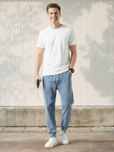 Jeune homme caucasien souriant vêtu d'un jean élastique taille et chevilles en denim streetwear tendance bleu clair dans un lieu éclairé.