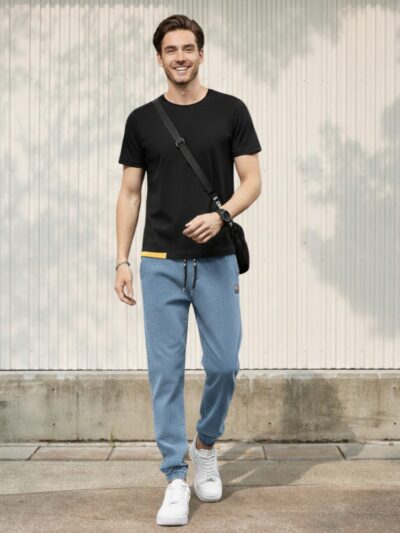 Homme caucasien brun portant un jean taille élastique bleu en denim doté d'une coupe jogger urbaine sur fond ensoleillé.