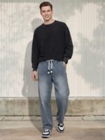 Homme caucasien vêtu d'un pull foncé et d'un jean taille élastique denim bleu clair à motif chevron sur fond clair et ensoleillé.