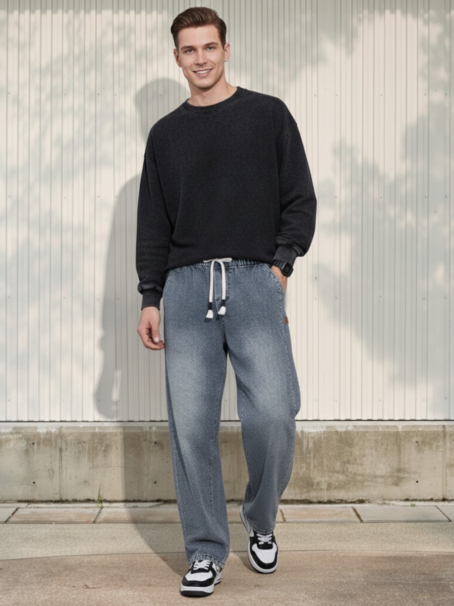 Homme caucasien vêtu d'un pull foncé et d'un jean taille élastique denim bleu clair à motif chevron sur fond clair et ensoleillé.