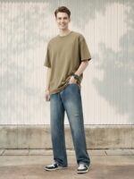 Jeune homme caucasien portant un jean skater bleu vintage délavé sur fond clair et ensoleillé.