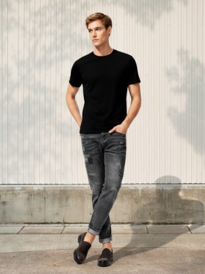 Jeune homme portant un t-shirt noir et un jean fuselé homme au confort stretch et tendance dans un lieu clair et ensoleillé.