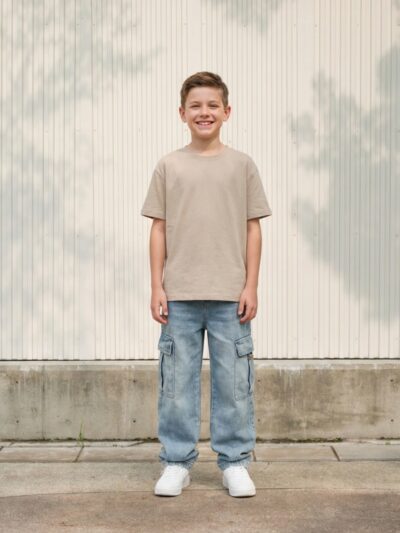Petit garçon portant un t-shirt beige avec un jean baggy bleu ciel à poches cargo, sur fond clair