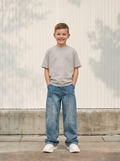 Petit garçon portant un t-shirt gris avec un jean baggy délavé bleu, sur fond clair