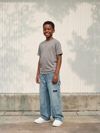 Petit garçon portant un t-shirt gris avec un jean baggy bleu délavé, sur fond clair