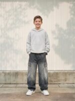 Petit garçon portant un sweat gris avec un jean baggy gris délavé, sur fond clair