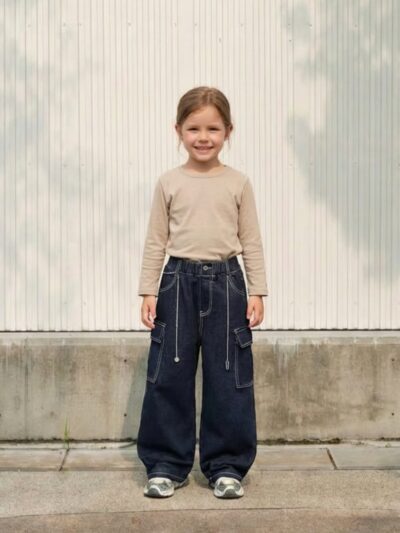 Petite fille portant un haut beige avec un jean cargo bleu brut, sur fond clair