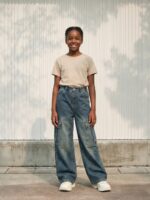 Petite fille portant un t-shirt beige avec un jean cargo bleu délavé d'inspiration vintage, sur fond clair