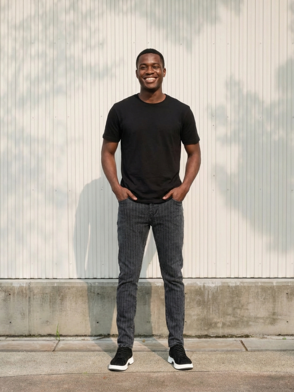 Homme portant un t-shirt noir avec un jean gris anthracite à rayures, sur fond clair