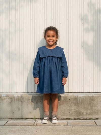 Petite fille portant une robe en jean à col marin et manches bouffantes, sur fond clair