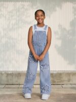Petite fille portant une salopette en jean bleu ciel avec des motifs étoiles, sur fond clair