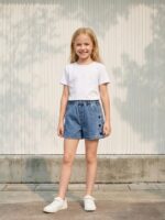 Petite fille portant un t-shirt blanc avec un short en jean bleu à coeurs, sur fond clair