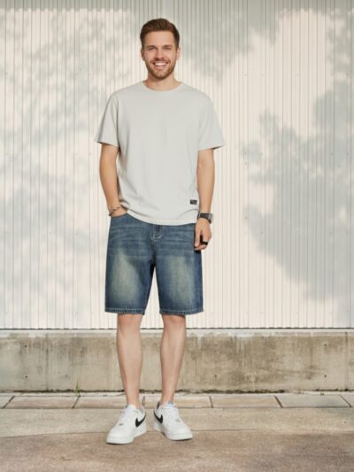 Homme portant un t-shirt beige avec un short en jean bleu délavé de style vintage, sur fond beige