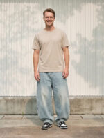 Homme portant un t-shirt beige avec un jean ballon bleu clair délavé, sur fond beige