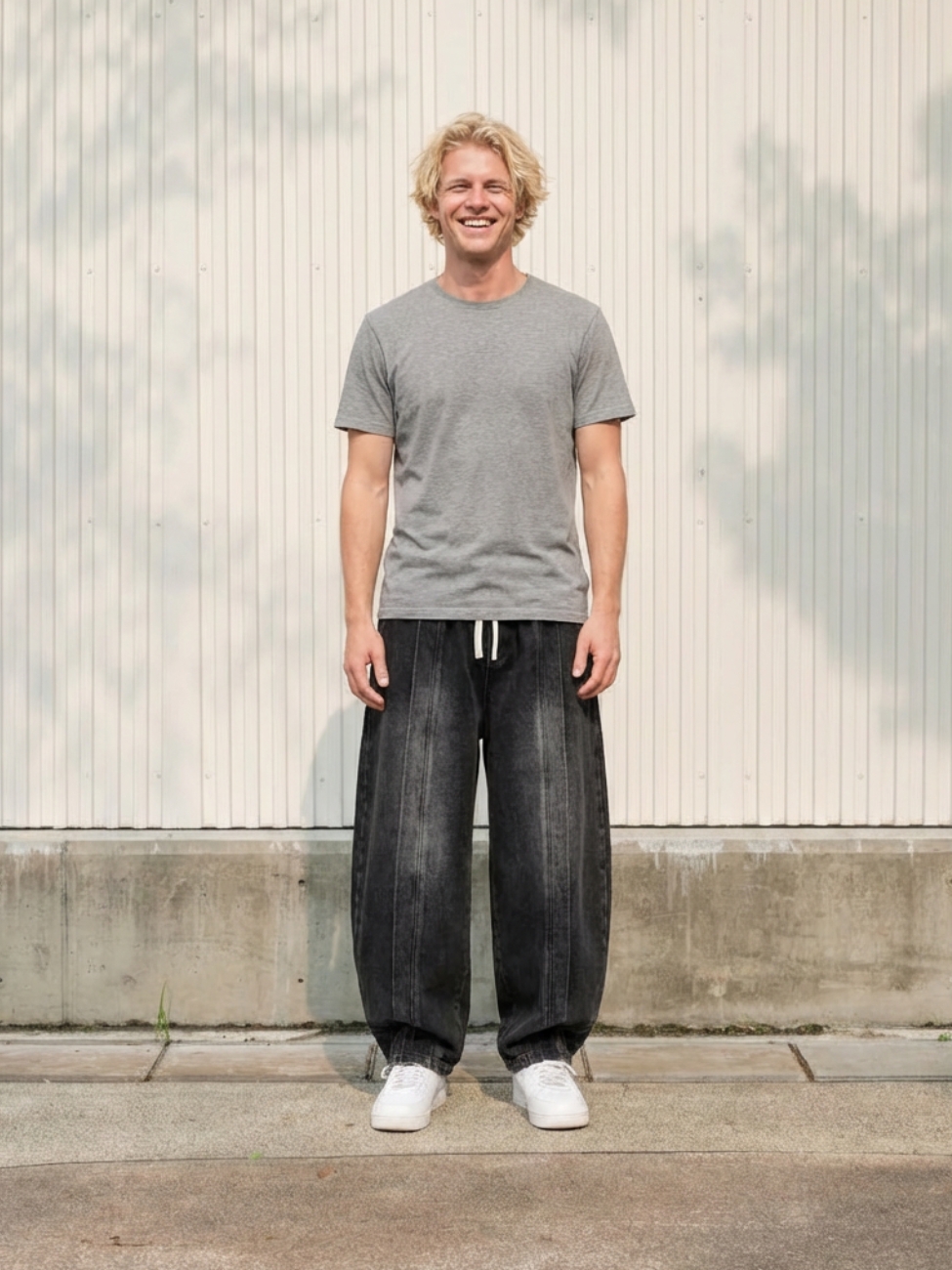 Homme portant un t-shirt gris avec un jean ballon noir délavé, sur fond beige