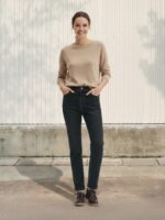 Femme portant un pull beige avec un jean court en denim noir, sur fond beige