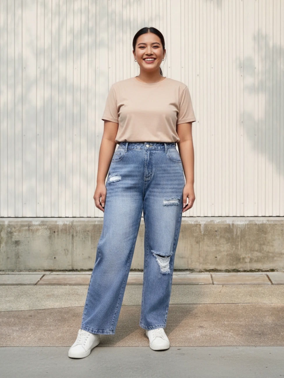 Femme portant un t-shirt beige avec un jean bleu troué grande taille, sur fond clair